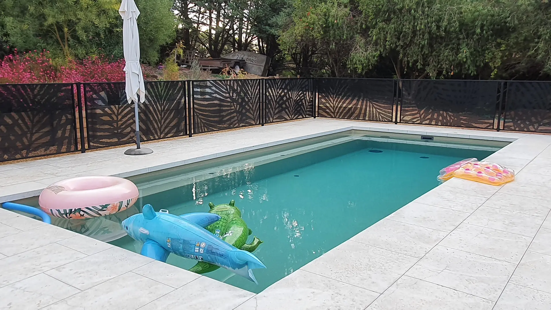 A pool with inflatable pool toys in it, and a Palmy Perf design PoolPerf&reg; pool fence running along the back