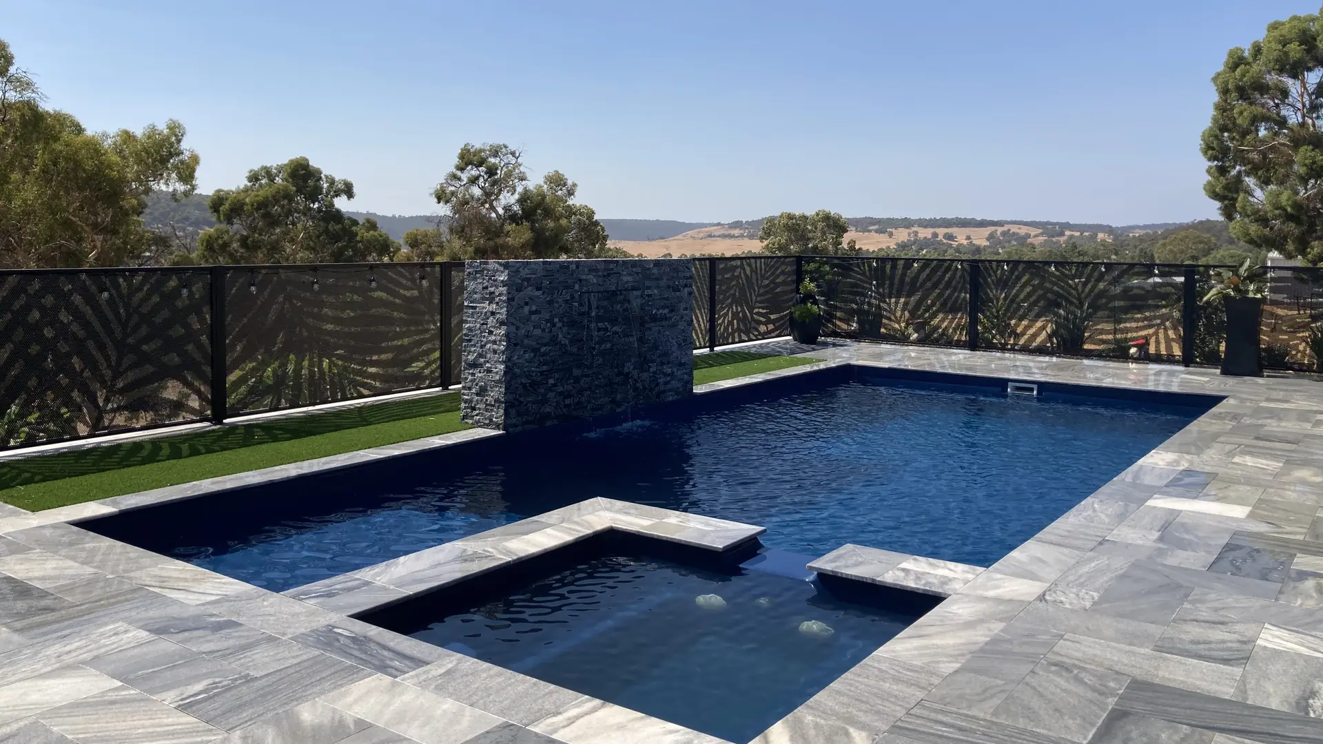 A Palmy Perf design PoolPerf&reg; pool fence around a hilltop pool, with the hills showing through it