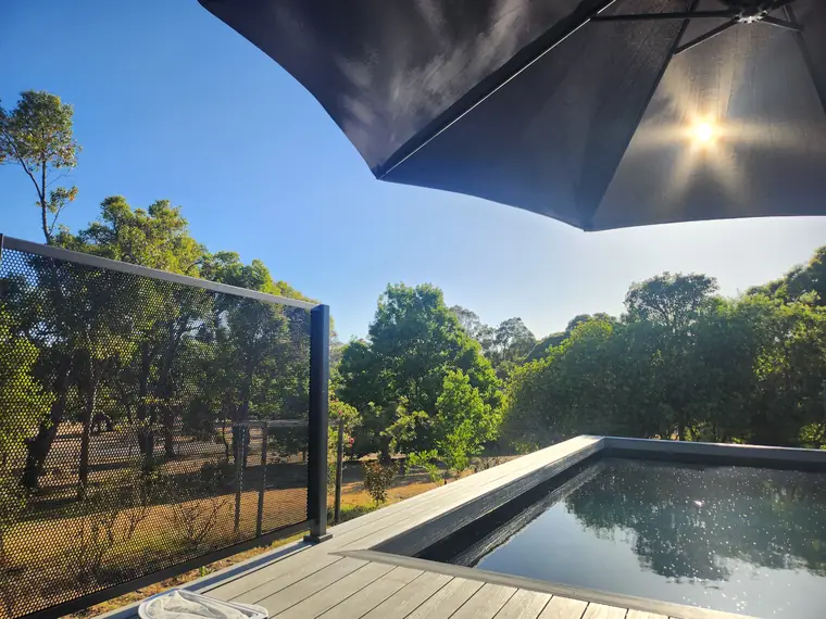 A PurePerf panel on the edge of a raised pool deck in Western Australia, with bushland beyond and the pool reflecting the trees