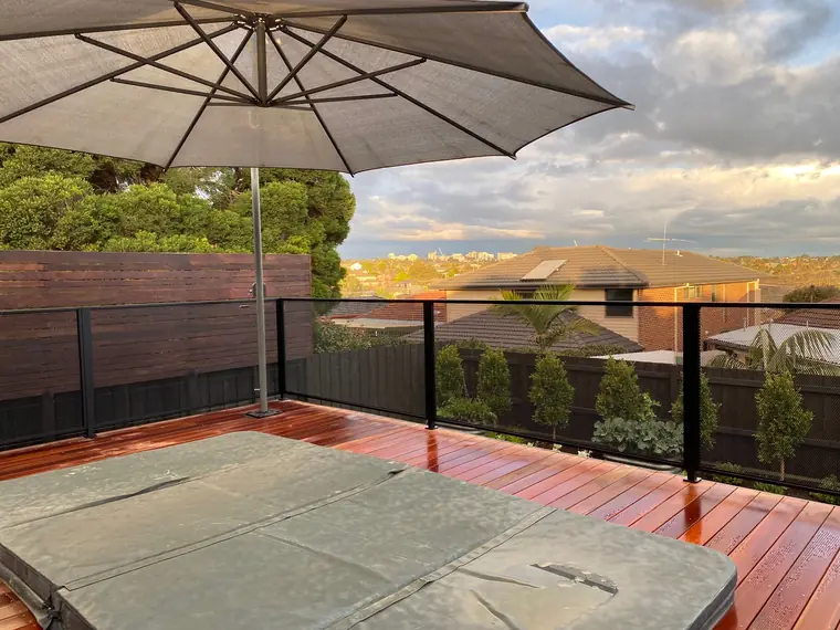 A spa on a raised timber deck with a black PurePerf balustrade, an umbrella and a view over the rooftops to a city skyline