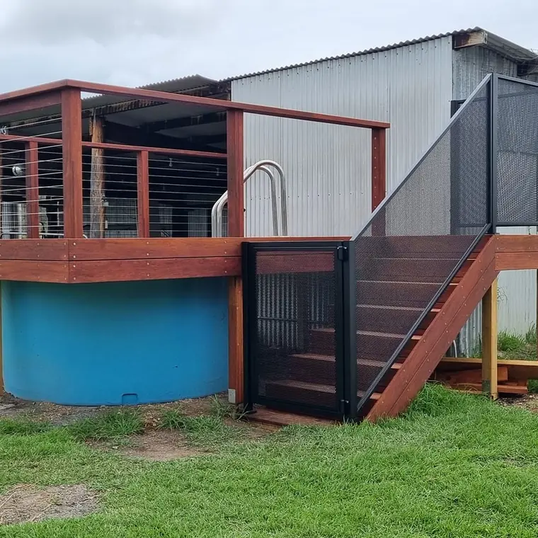 A round tank pool on a New South Wales farm with a timber deck around it, and black PurePerf panels on the stairs and gate up to the deck