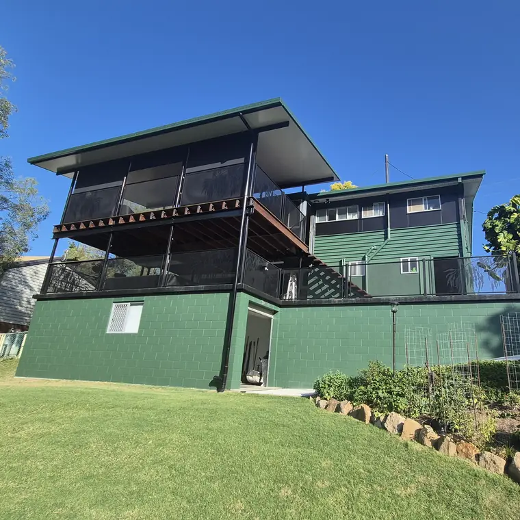 A green three-level home in Queensland with black Gum Perf balustrades on two deck levels and the stairs between them