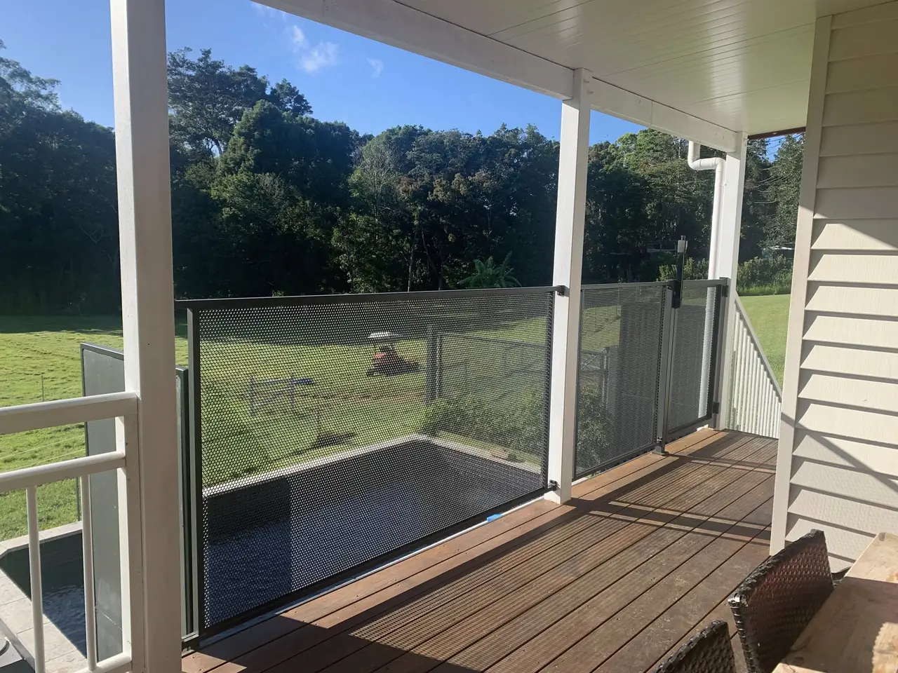A covered timber verandah in Queensland with a Monument grey perforated balustrade and gate along its edge, and a plunge pool on the level below