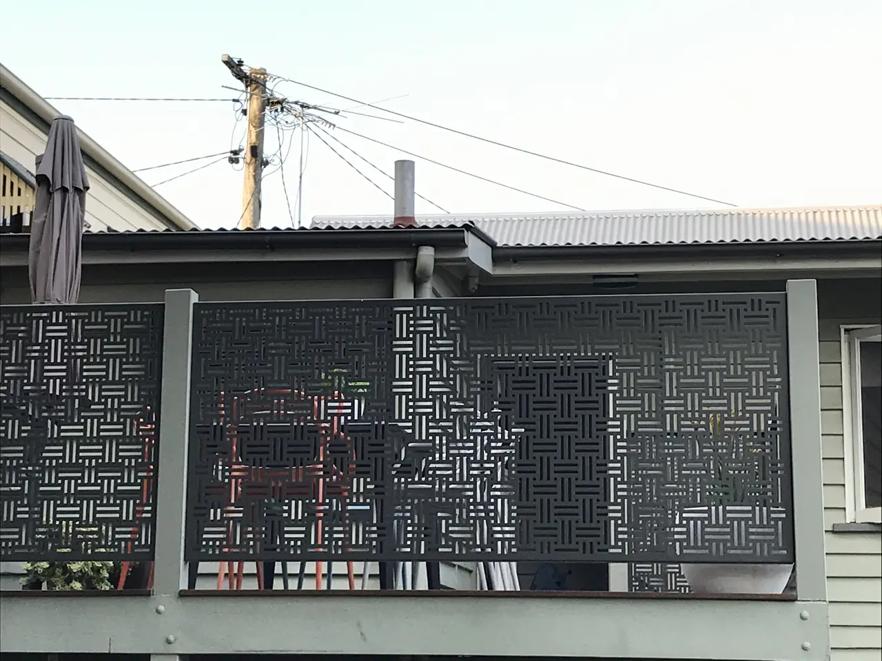 The timber deck of a Queensland home with a Weave custom design perforated balustrade in Woodland Grey between grey posts