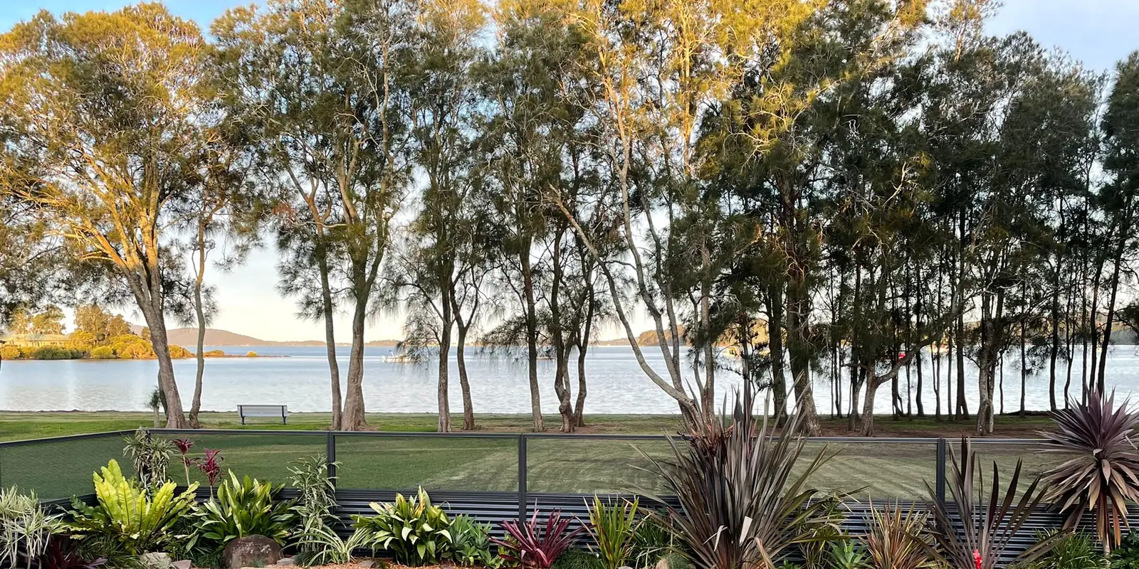 A lawn, tall trees and a lake beyond, seen through a perforated sheet that is black on one side and white on the other