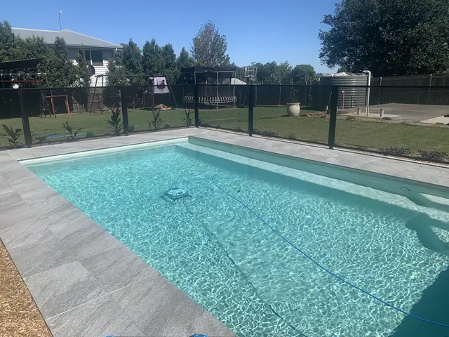 A black PurePerf pool fence around a bright pool, with paving and a lawn behind