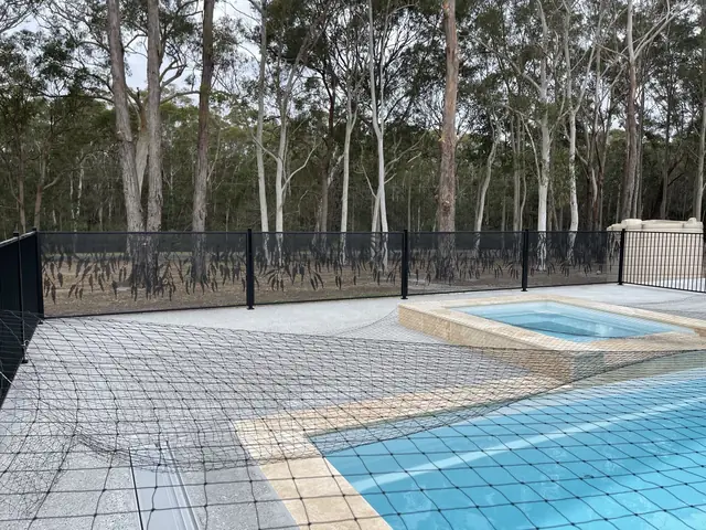 A black Gum Perf design pool fence with tall gum trees behind, beside a pool and spa