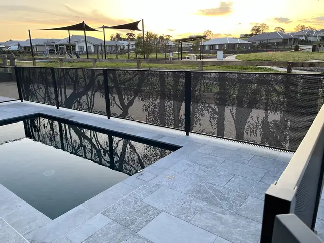 A black one-off custom fence with tree silhouettes, beside a dark pool at sunset