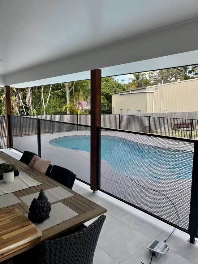 A black PurePerf fence beside an outdoor table, with a kidney-shaped pool behind it