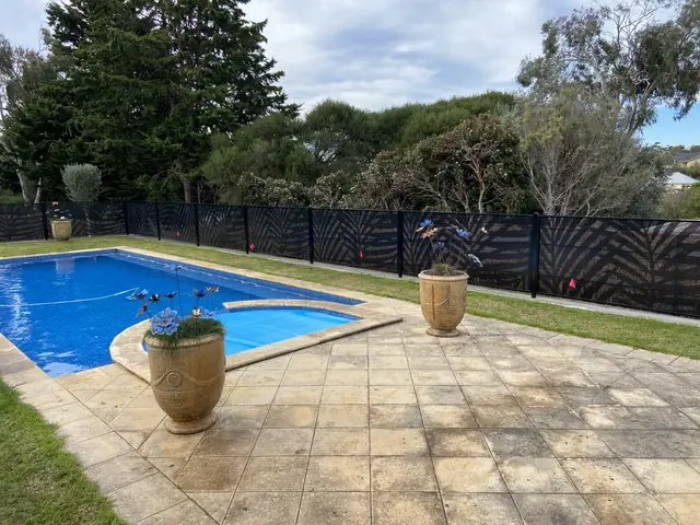 A black Palmy Perf design fence around a pool with a paved surround