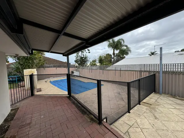 A black PurePerf fence under a carport roof, beside a covered pool