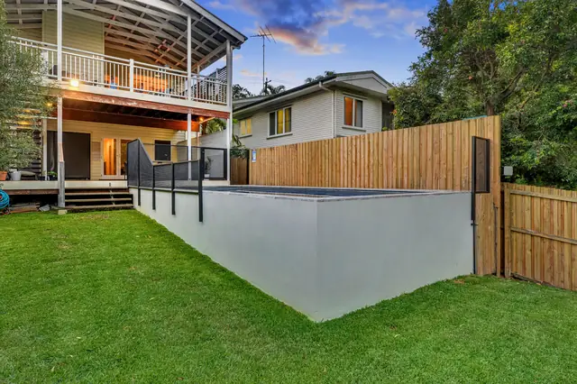 A black PurePerf fence on top of a raised pool wall beside a lawn