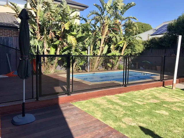 A black PurePerf fence on a timber deck, with a pool and banana palms behind