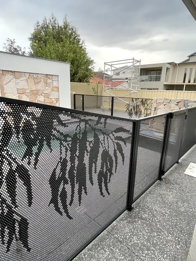 A black Gum Perf design fence beside a stone wall
