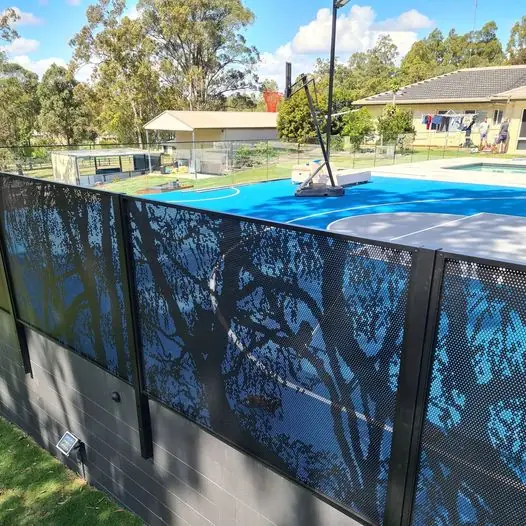 A black one-off custom fence with tree silhouettes, a bright pool behind it