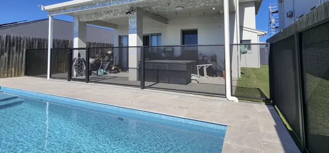 A black PurePerf fence between a pool and a covered outdoor area