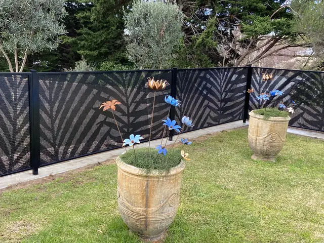 A black Palmy Perf design fence in a garden with flower pots