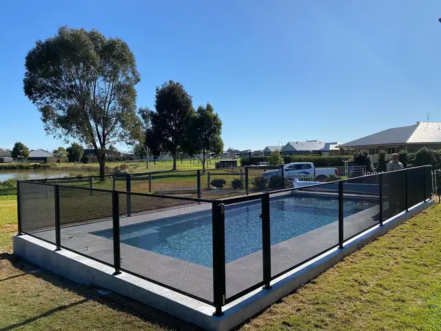 A black PurePerf fence around a pool on a raised slab, with a lake and gum trees behind