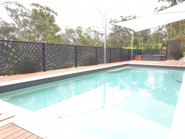 A black Palmy Perf design fence behind a pool and a shade sail