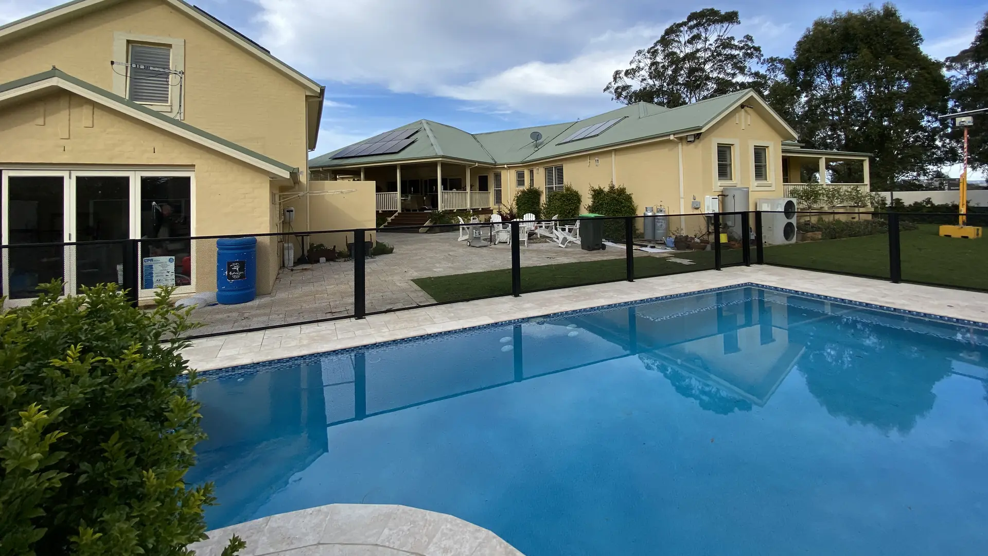 A black PurePerf pool fence around a pool beside a two-storey cream weatherboard house