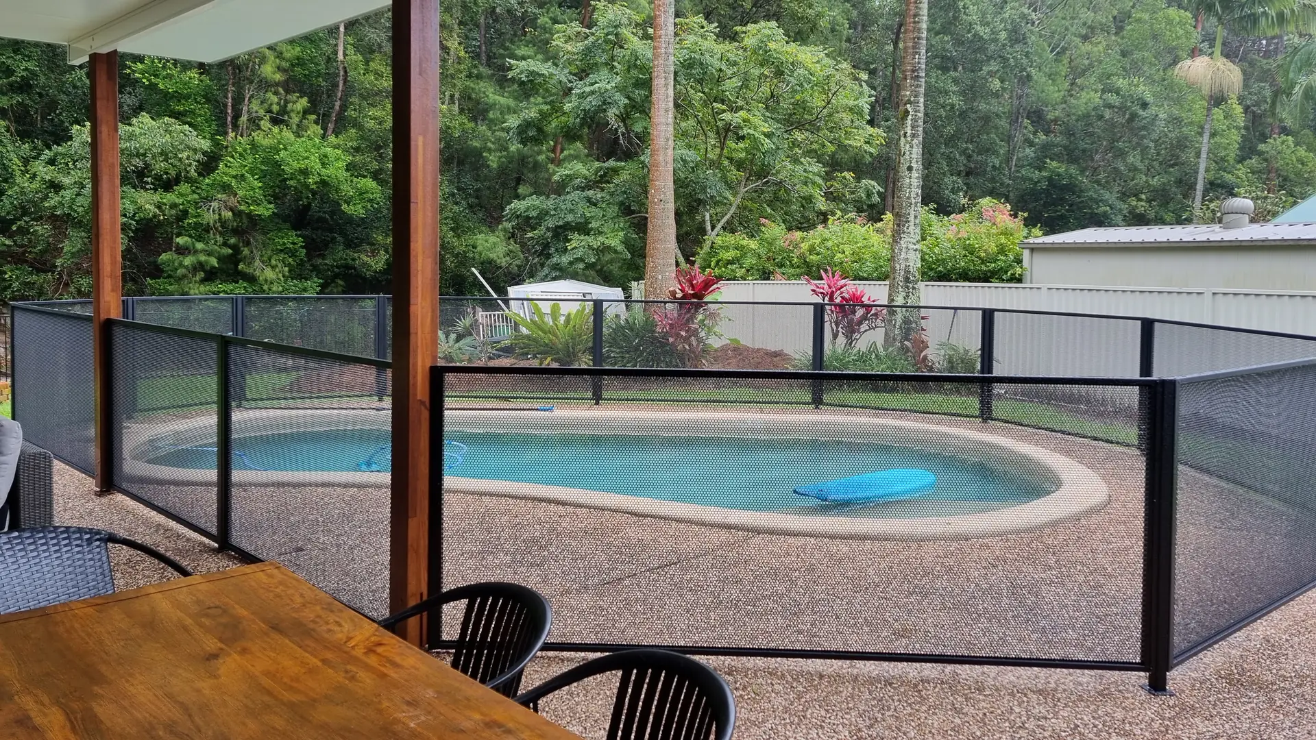 Looking from a covered patio through a black PurePerf fence to a kidney-shaped pool and a rainforest garden