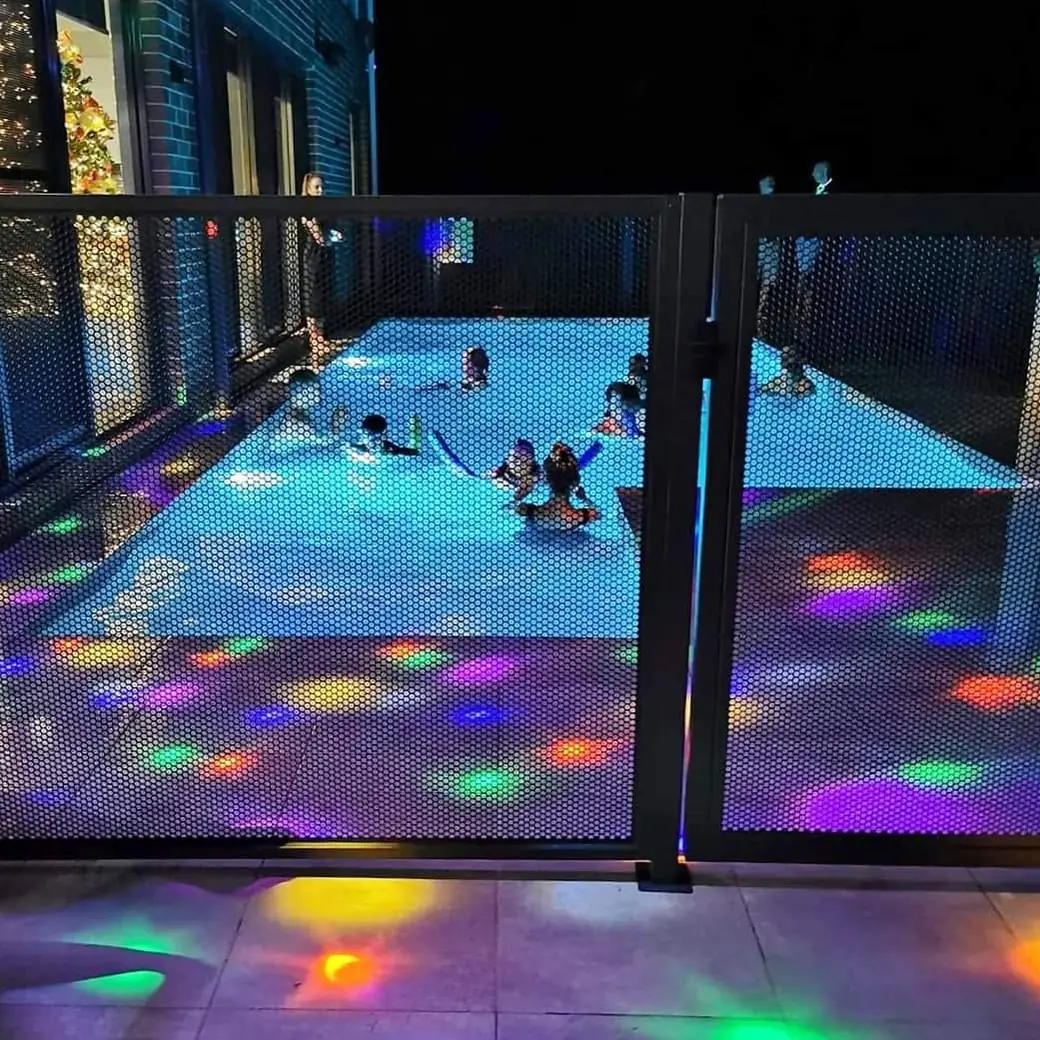 The family pool at night with children swimming and coloured disco lights shining through the black PoolPerf fence