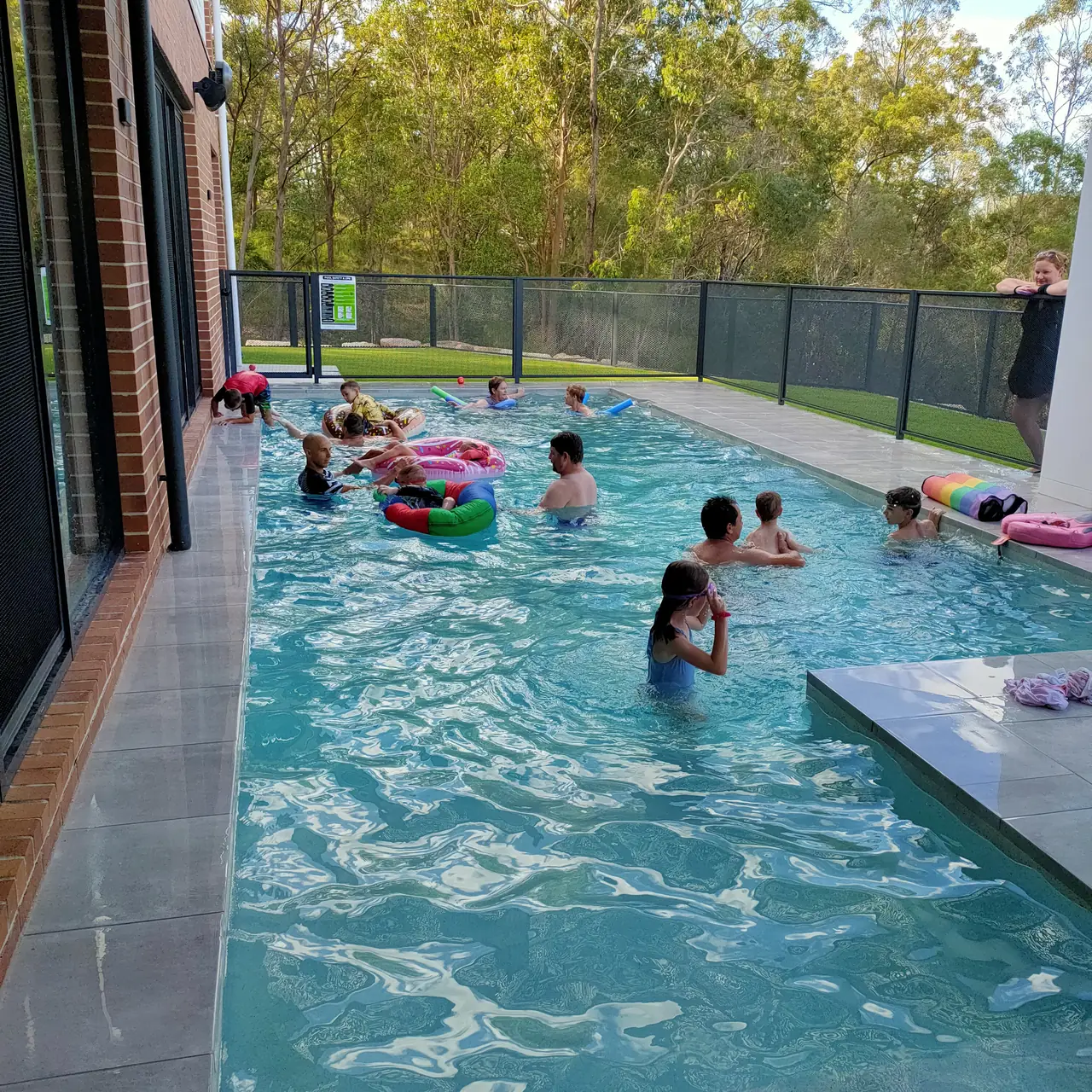 Children swimming in the long family pool on a sunny afternoon, with the Monument grey PoolPerf fence along the far side