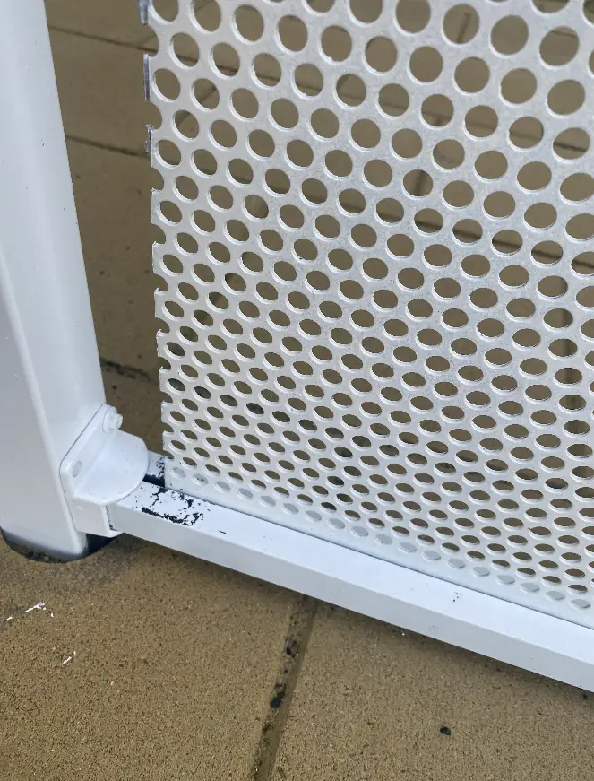 The bottom corner of an imported perforated panel against its post, with paint chipped off at the join