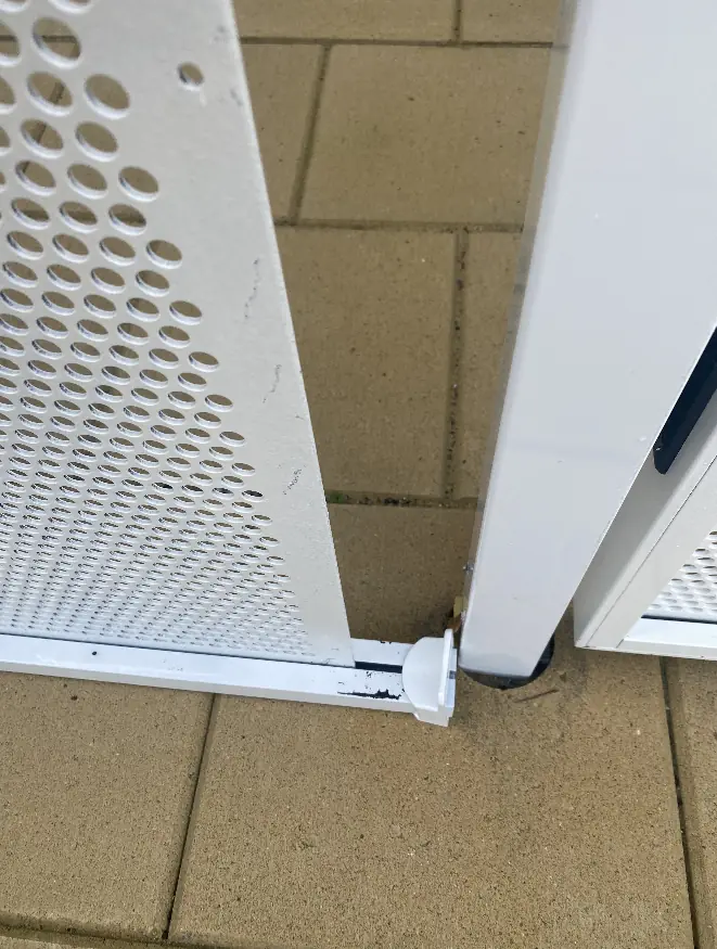 The bottom corner of an imported perforated gate, with the bottom rail and the sheet coming apart and chipped paint
