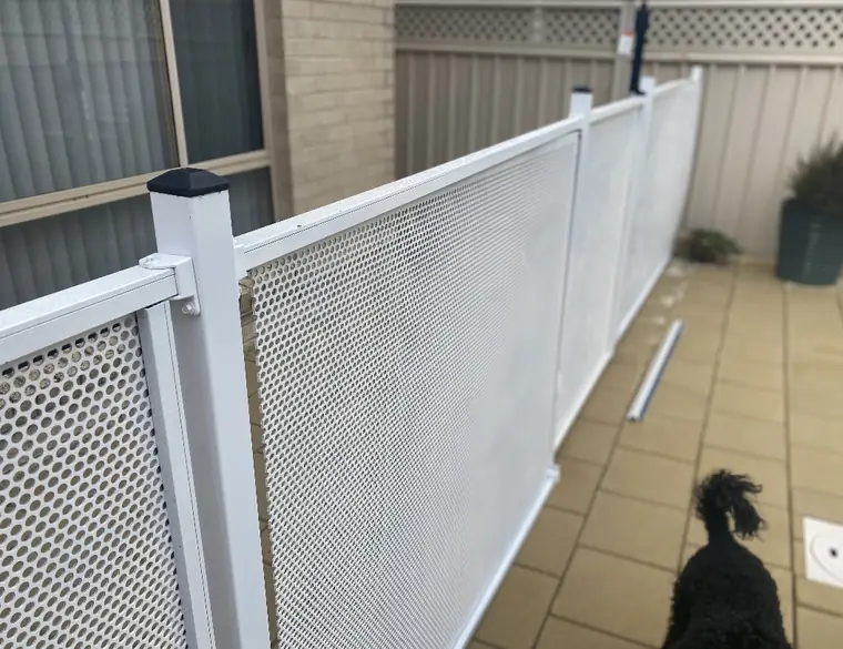 A run of imported white perforated fencing along a courtyard, with a loose length of rail lying on the pavers