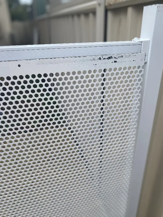 An imported perforated panel that has popped out of its frame below the top rail, with the paint finish damaged along the edge