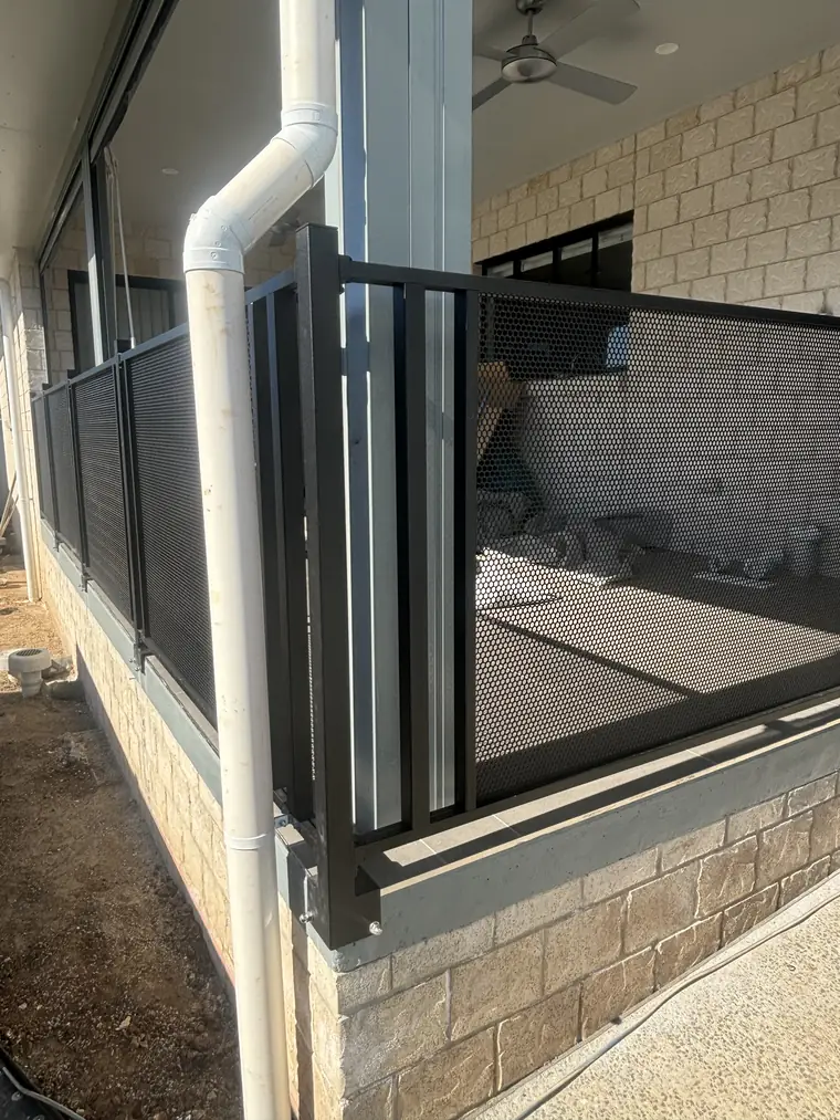 Black PoolPerf panels on custom posts fixed to the side of a raised patio slab beside a downpipe