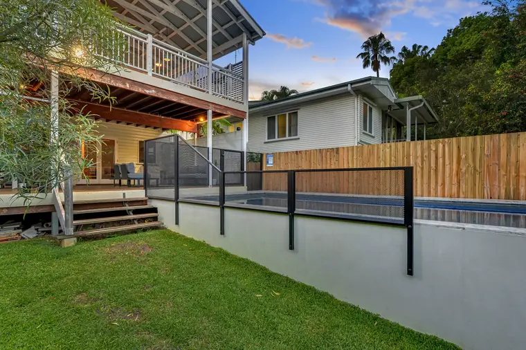A pool built up behind a rendered retaining wall on a sloping lawn, with black PoolPerf posts fixed to the face of the wall