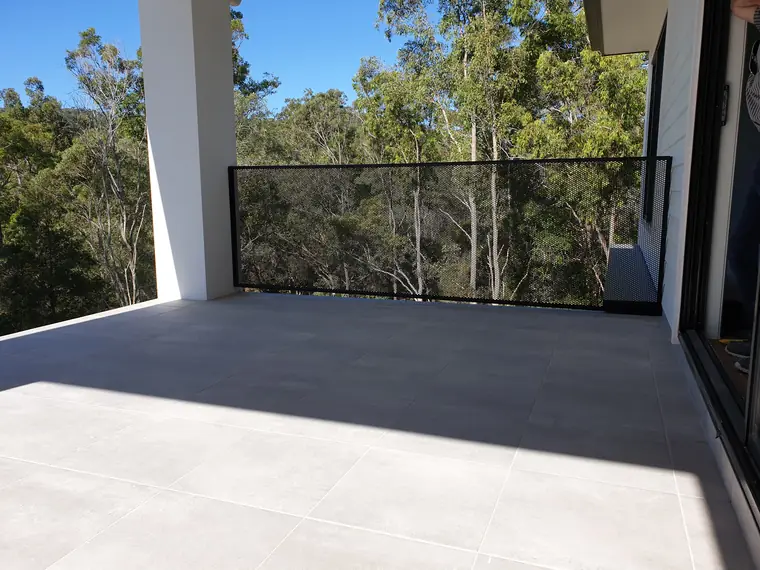 A single long black PoolPerf panel along the edge of a tiled terrace, with gum trees beyond
