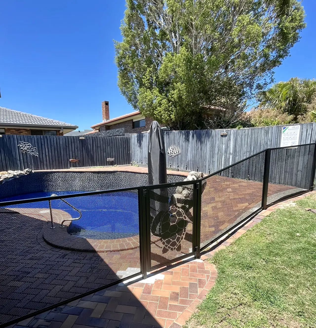 Black PoolPerf panels following a sloping lawn beside a curved brick pool path, with a turtle design gate