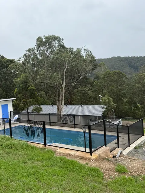 Black PoolPerf panels following a grassy slope beside a pool, with a tall gum tree and hills behind