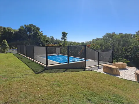 A black PoolPerf fence around a pool set into a sloping lawn, with large garden rocks at the lower corner