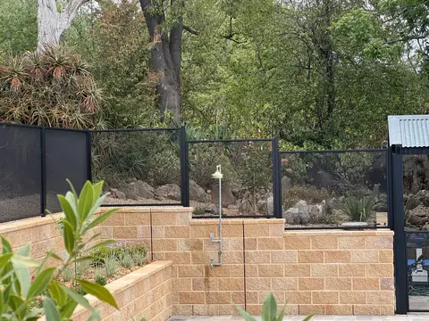 Black PoolPerf panels on top of a sandstone coloured block retaining wall, stepping down where the wall steps down