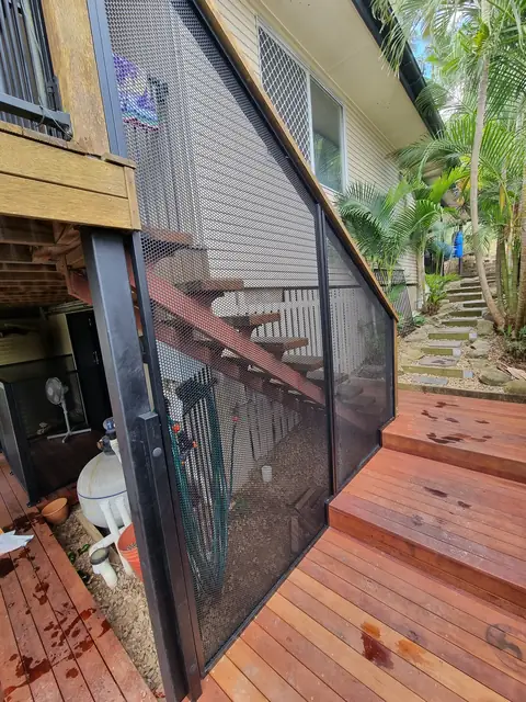 Black PoolPerf panels fitted under and beside a timber deck staircase, shaped around the bottom step