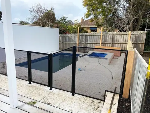A black PoolPerf fence around a pool and spa, with one panel cut to step up over a raised concrete edge