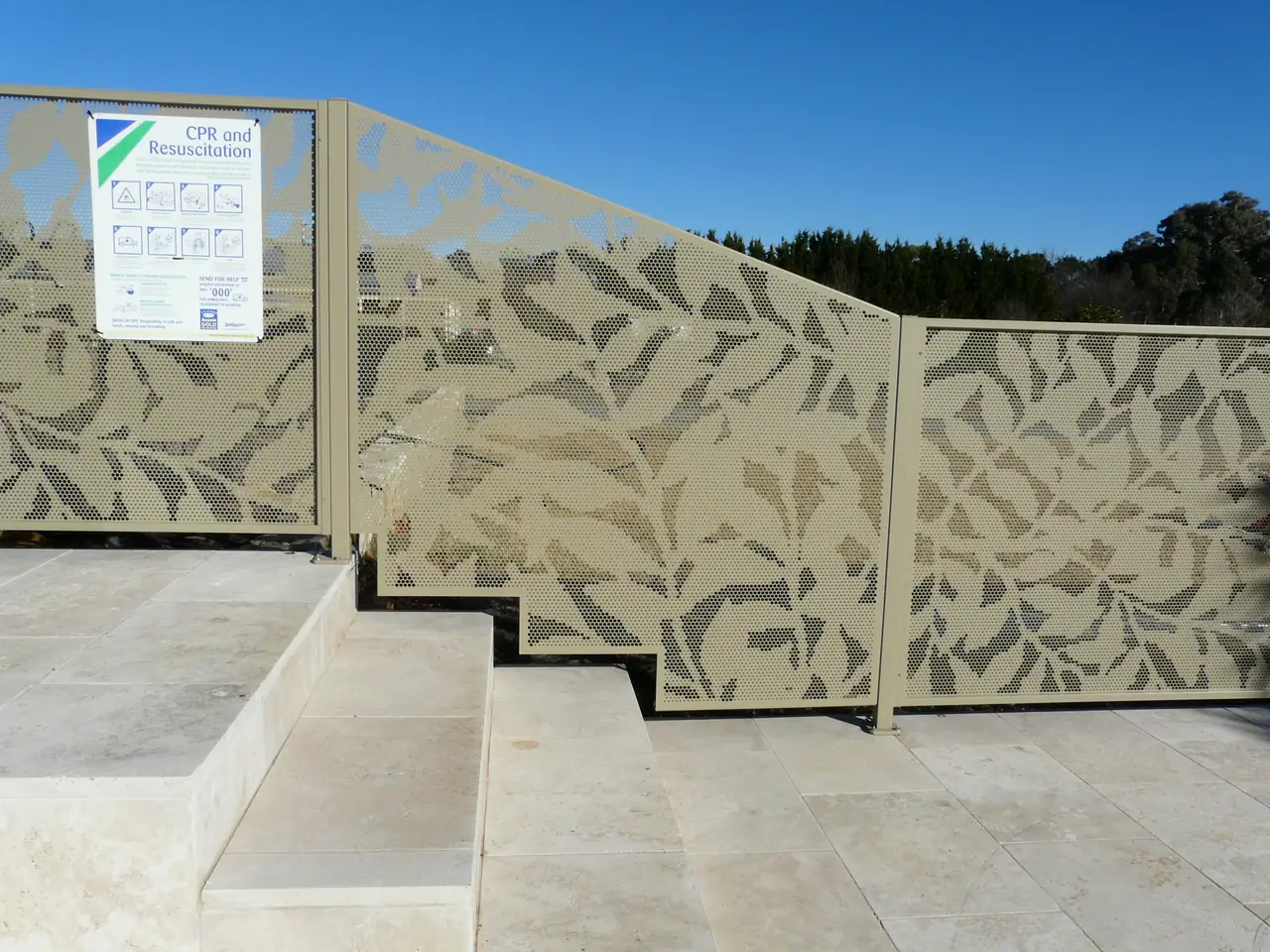 A light coloured Ficus design PoolPerf panel beside pool stairs, its bottom cut in three steps to follow the stairs and its top sloping down to the next panel