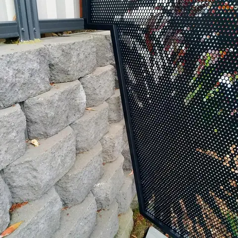 Close up of a black Pandanus design PoolPerf panel whose edge is cut on an angle to sit against a sloping block retaining wall