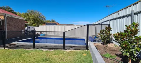 A black PoolPerf fence beside a pool that rises with a transition panel to meet a tall boundary fence next to a garden bed