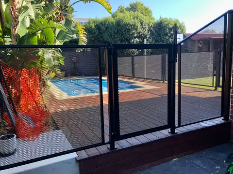 A black PoolPerf fence and gate on a timber pool deck, with a panel at the end whose top slopes up to a taller fence