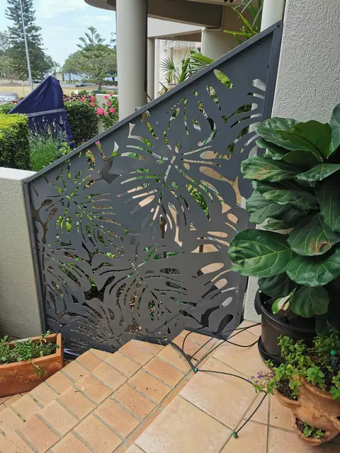 A grey Monstera 2 design panel beside brick entry steps, its top sloping down to follow the steps
