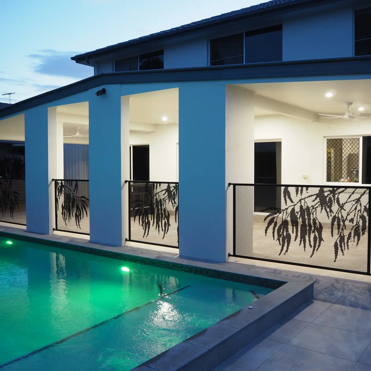 Black Gum design PoolPerf panels between the columns of a two storey home, beside a lit pool