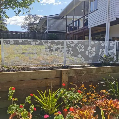 White Hibiscus design panels on top of a timber retaining wall above a garden bed of flowers