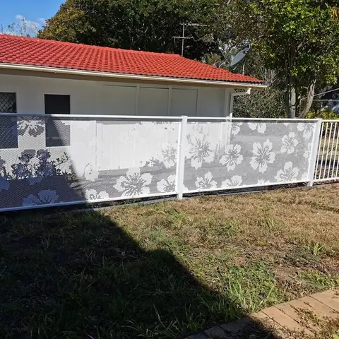 A white Hibiscus design fence along a lawn in front of a cottage with a red tiled roof