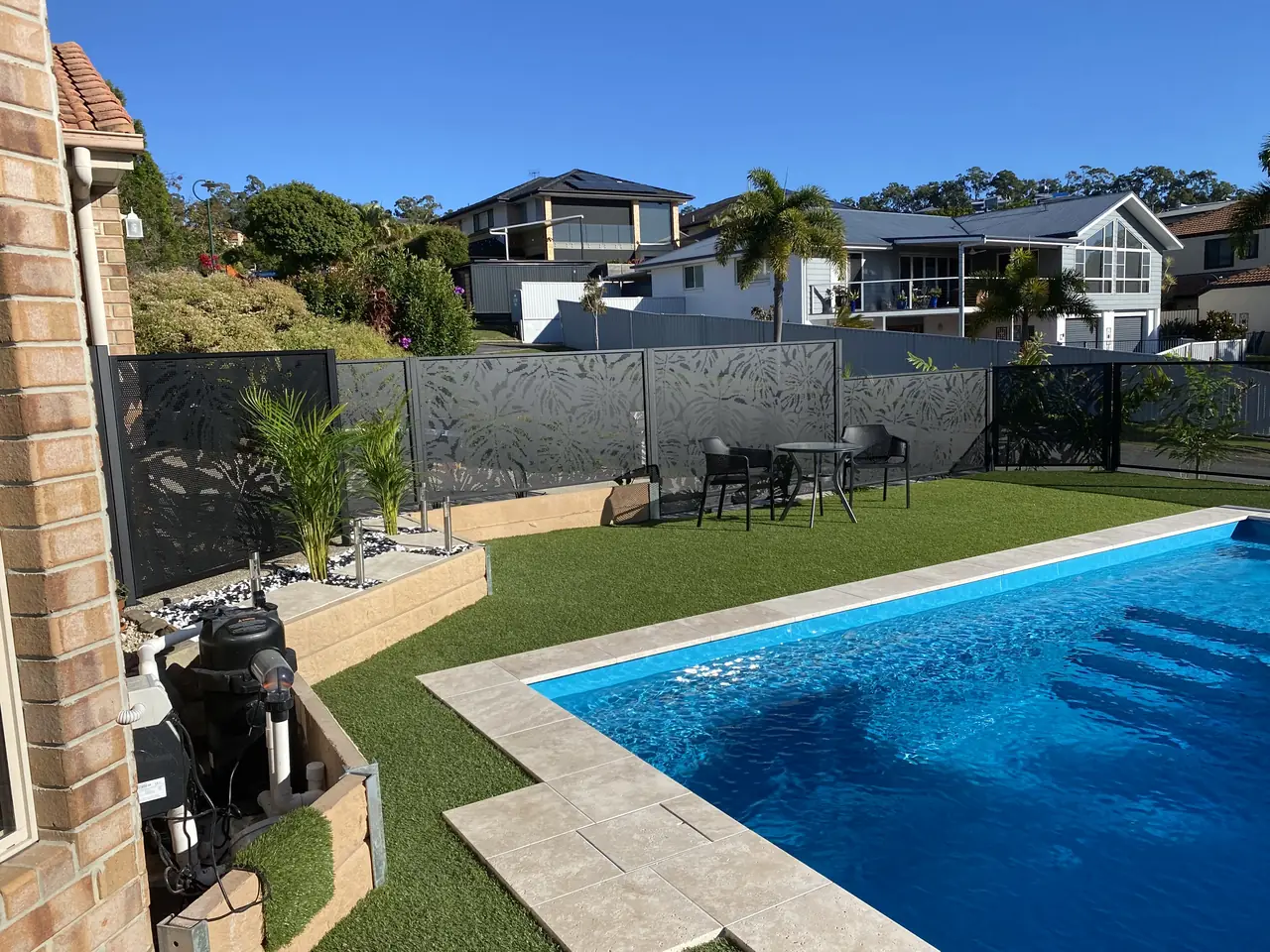 Black Monstera design panels along the back of a Queensland pool, with lawn and houses beyond