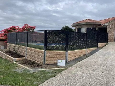 Black Monstera design panels on a raised garden wall, with red flowers above the fence
